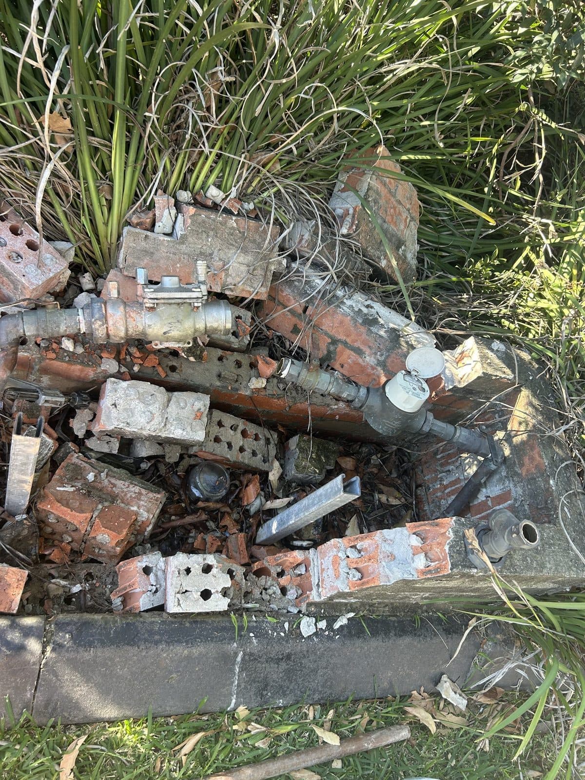 Broken water service among fallen bricks, with the meter and fittings damaged