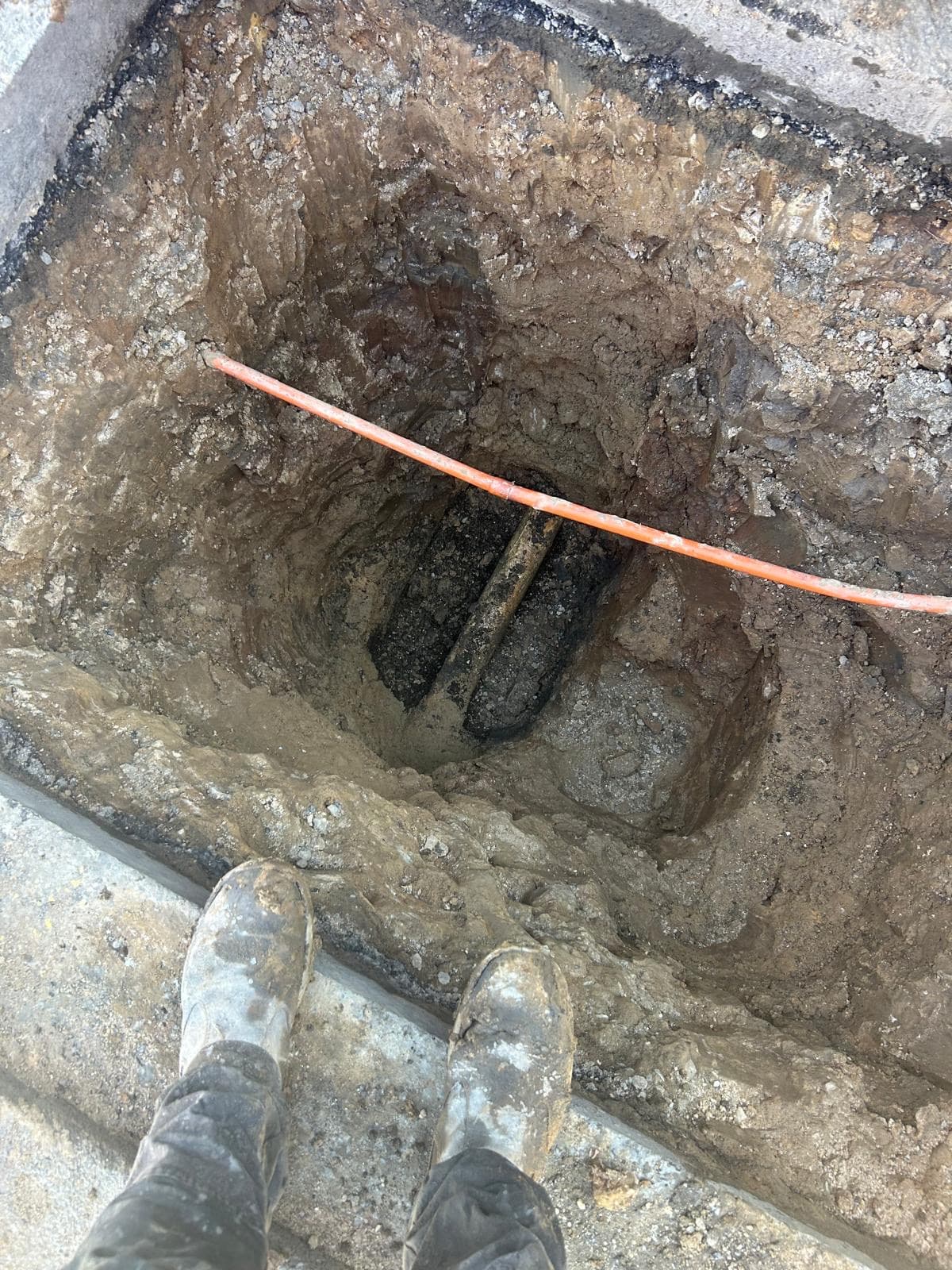 Excavated hole with an exposed pipe and orange marker tape