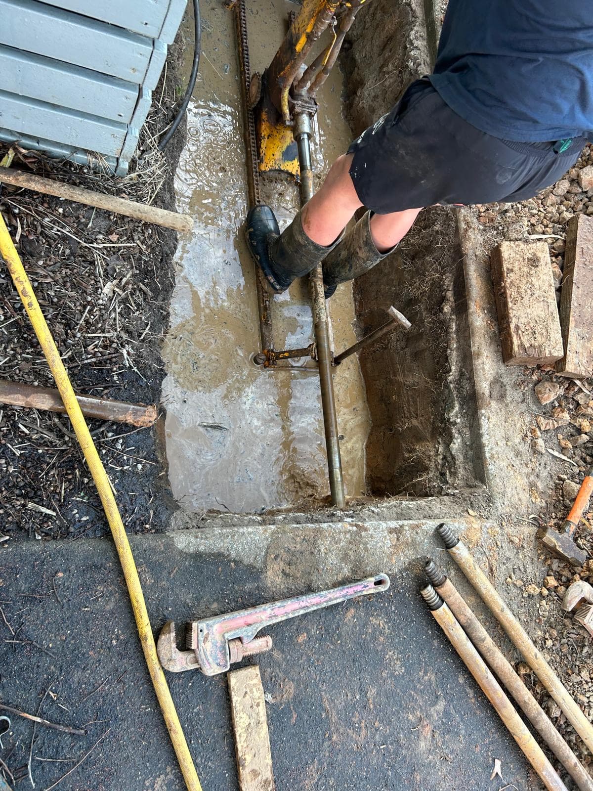 Work boots in a trench, with a pipe wrench and tools on the slab