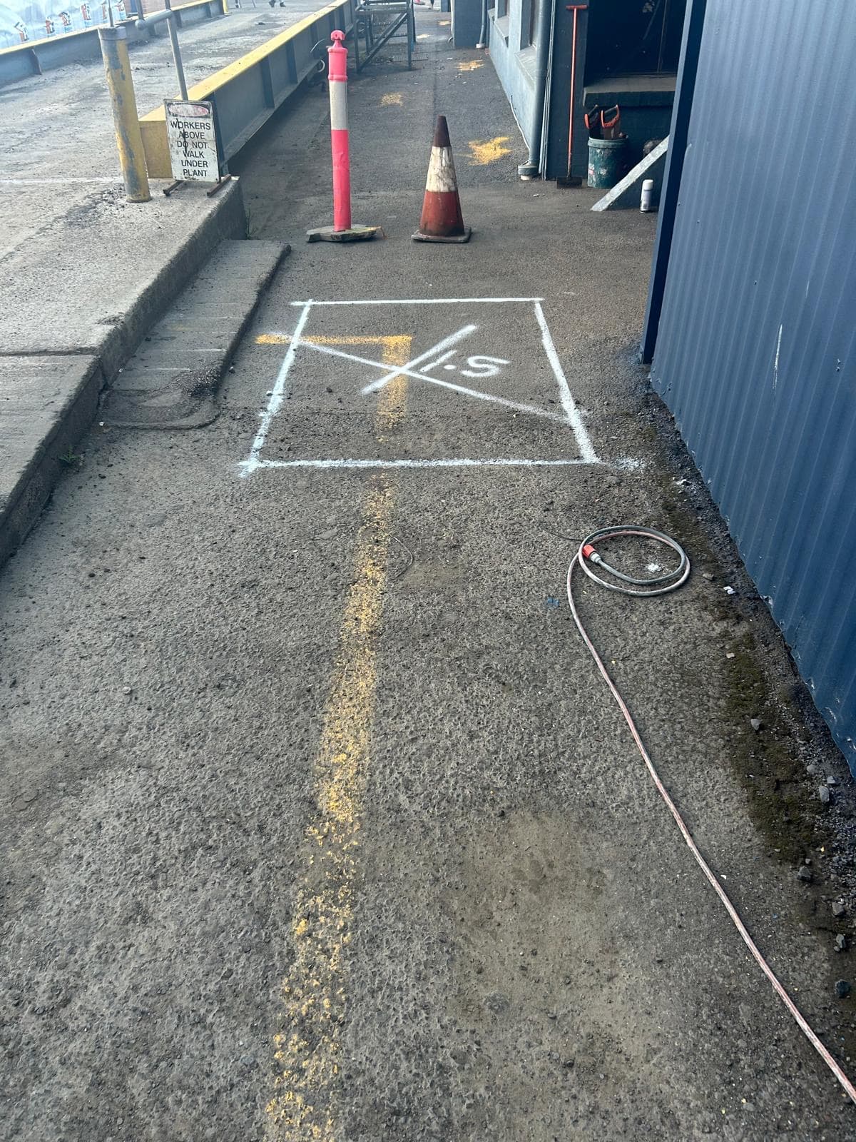 Square marked in paint on concrete with "1.5" beside it, and traffic cones