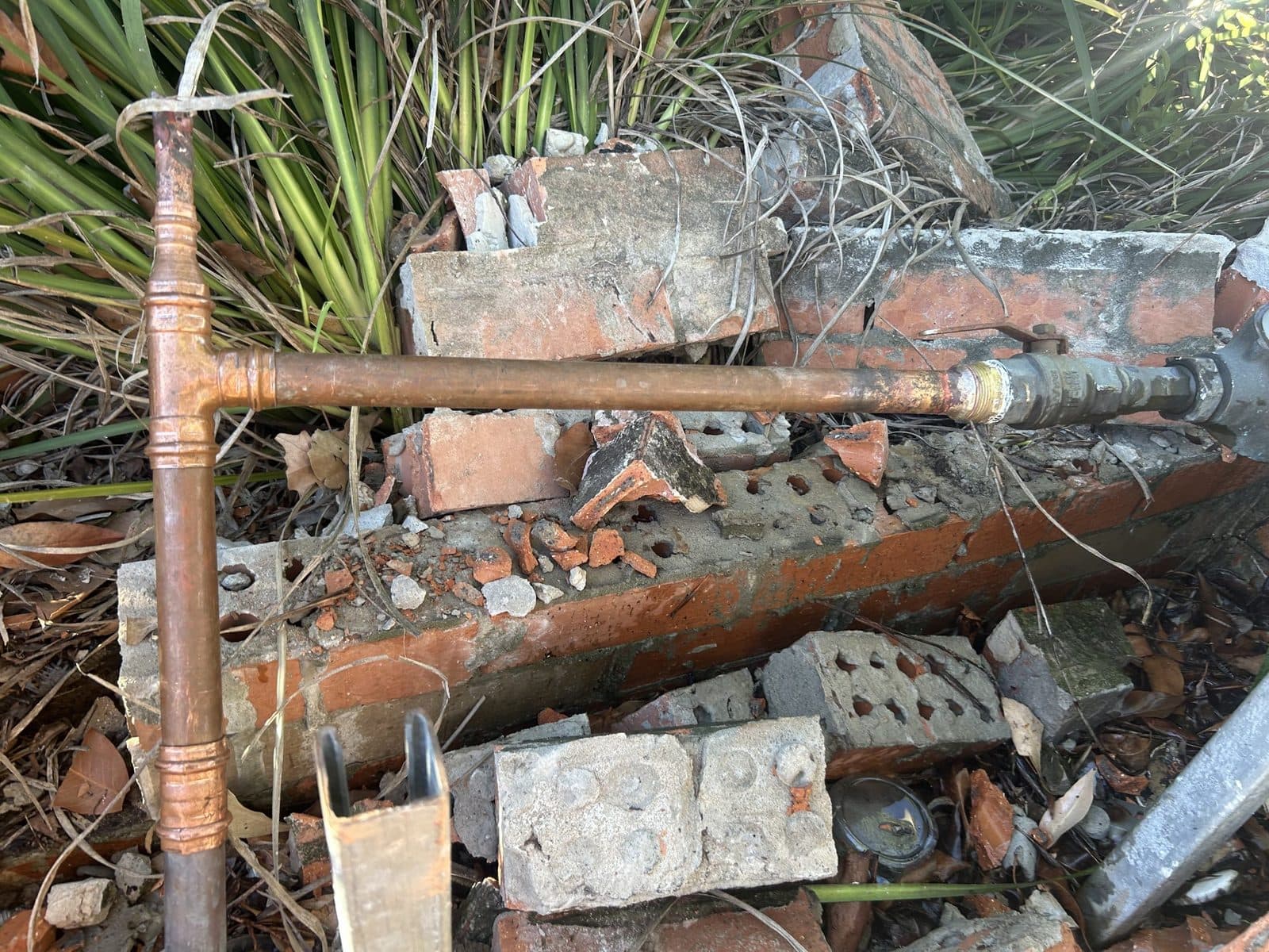 New copper pipework joined onto an older line beside a broken brick wall