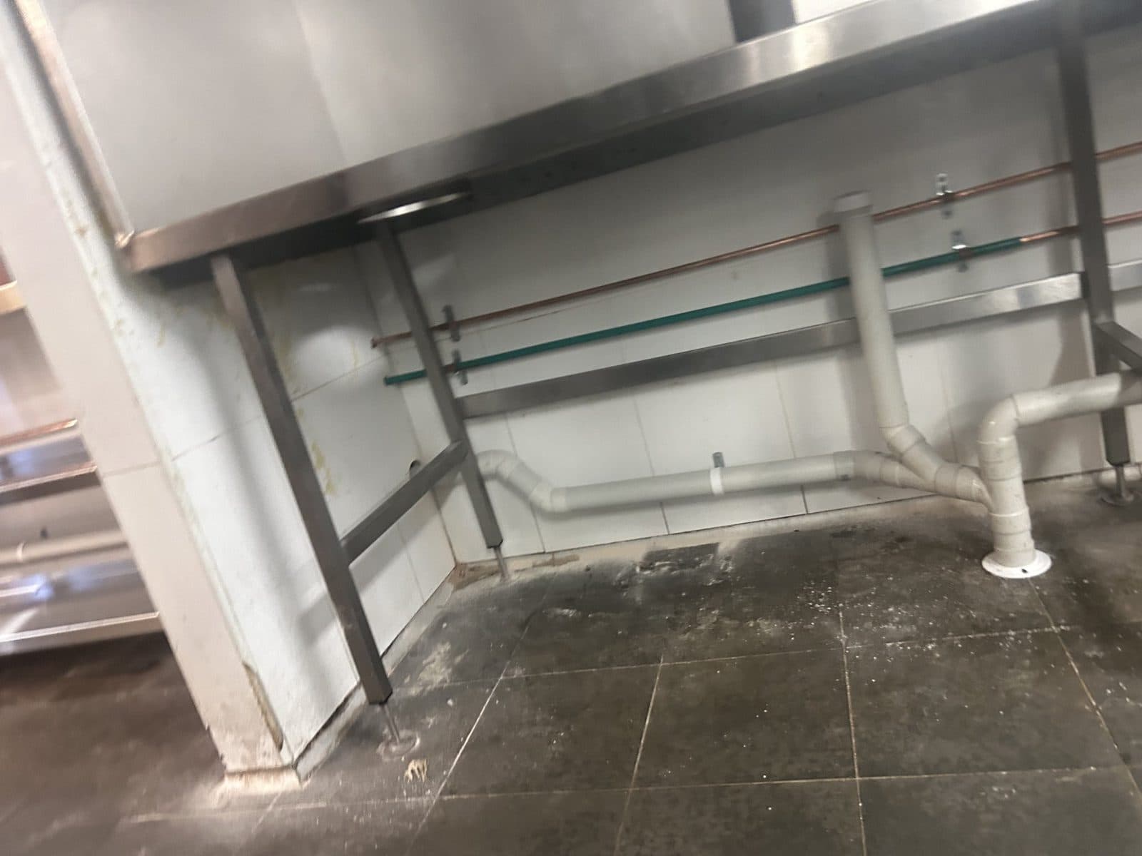 Copper lines and white waste pipes under a stainless bench