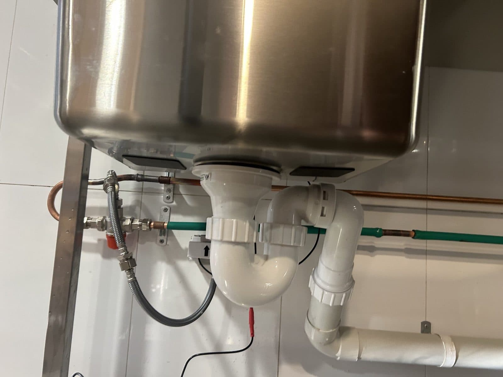 Waste trap, copper lines and a braided hose under a stainless sink